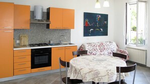 Una cocina con armarios color naranja, una estufa y un lavabo. Hay una mesa de comedor con sillas y un cuadro en la pared.