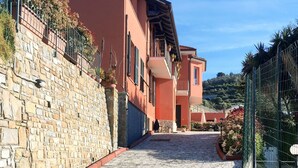 Una calle adoquinada que lleva a un edificio, con un muro de piedra a un lado y una valla al otro.