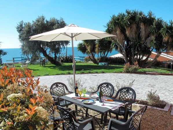 An outdoor patio with a table and chairs, a white umbrella, and a view of the ocean. - Cosy apartment for 5 guests with WIFI, TV and patio (Imperia)