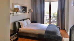 A hotel room with a large bed, a nightstand, a lamp, a framed picture, and a balcony with curtains.