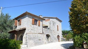 A stone building with a tiled roof, arched windows, and wooden shutters.