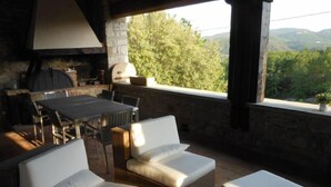 An outdoor patio with wicker furniture, a stone wall, and a view of the countryside.