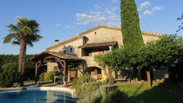 A stone villa with a swimming pool, a pergola, and a tall cypress tree.
