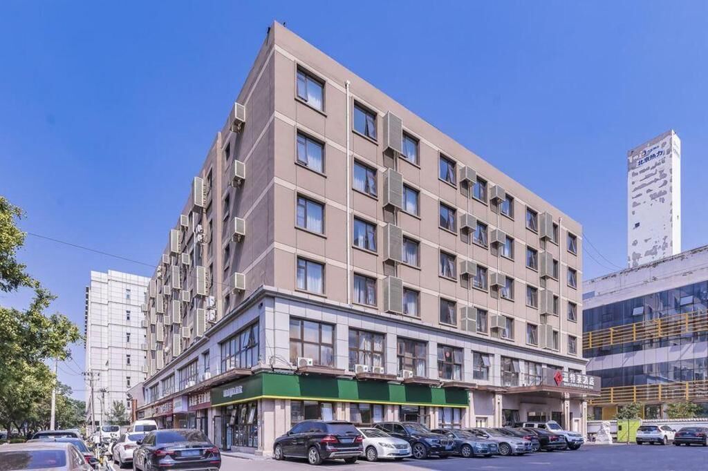 A multi-story hotel with a modern design, featuring a green awning and several air conditioning units on the facade.