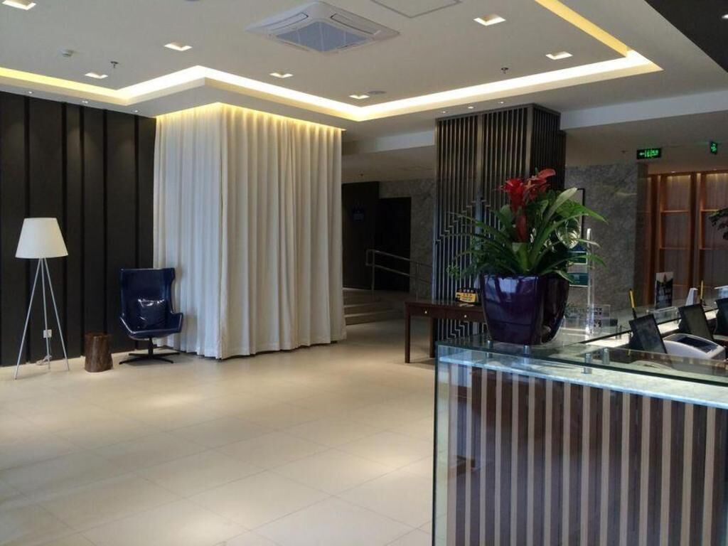 A modern lobby with a reception desk, a blue chair, a lamp, and a plant.