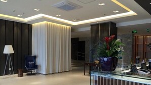 A modern lobby with a reception desk, a blue chair, a lamp, and a plant. - Jinjiang Inn (Beijing)