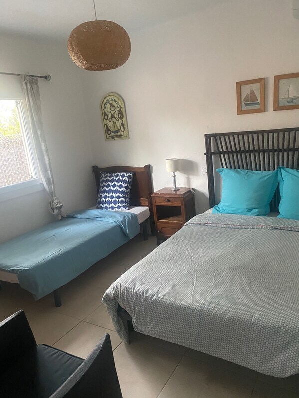 A room with two single beds, a wooden headboard, a small bedside table with a lamp, a wall-mounted decoration, and a window with curtains.