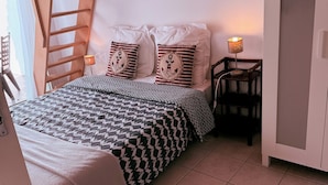 A bedroom with a bed, pillows, a nightstand, a lamp, a wardrobe, and a wooden ladder. - Air-conditioned villa with garden in the center of Marseillan (Marseillan)