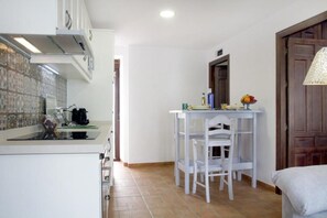 Une cuisine compacte avec des meubles blancs, un pare-feu en carrelage et un coin repas comprenant une table et des chaises blanches.
