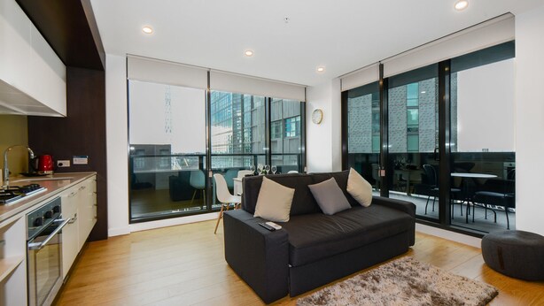 A modern living room with a dark sofa, a fluffy rug, and large windows offering a city view. - Opus tower (Southbank)