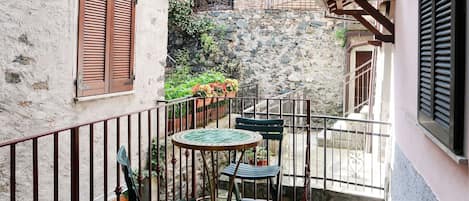 A small outdoor balcony with a round table and two chairs, surrounded by stone walls and a metal railing.