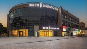 Um hotel moderno com fachada em vidro curvo, sinalização em vários idiomas e uma área de entrada ampla.