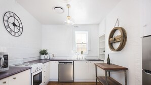 Eine moderne Küche mit weißen Schränken, Edelstahlgeräten, einer Holz Arbeitsplatte und einem runden Holzregal.