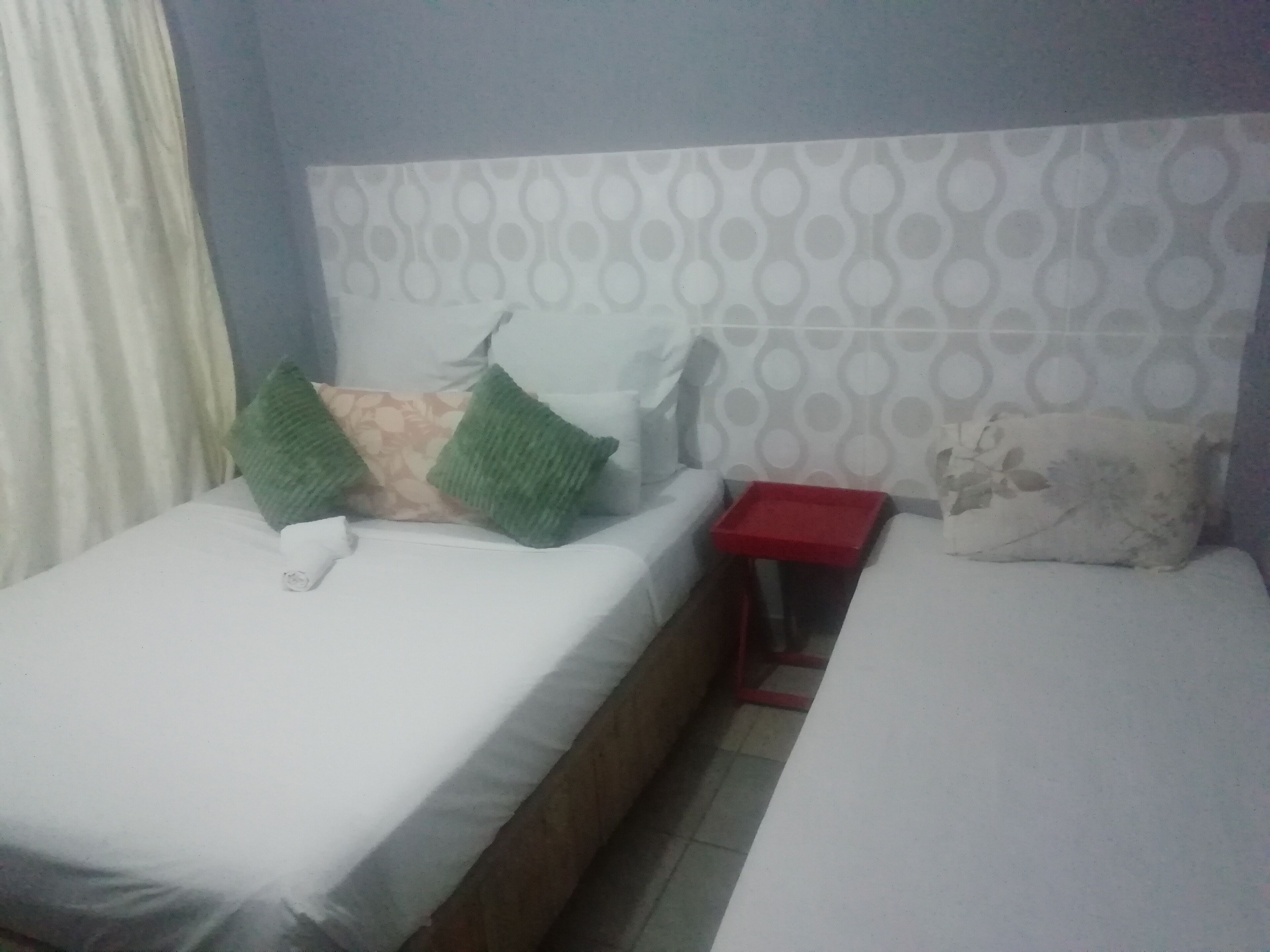 Ein Schlafzimmer mit zwei Betten, einem roten Nachttisch und einer Wand mit Muster.