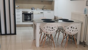 A modern kitchen with white cabinets, a dining area with white chairs, and a large window.