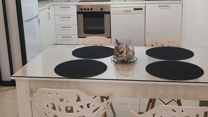A modern kitchen with white cabinets, a built-in oven, a dishwasher, and a dining table with two chairs.