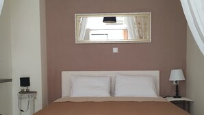 A bedroom with a bed, a bedside table with a lamp, a mirror, and a ceiling light fixture.