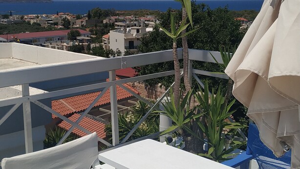 A balcony with a white table and chairs, a palm tree, and a view of a coastal town.