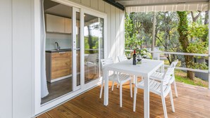 A covered outdoor dining area with a table and chairs, a view of a garden, and a sliding glass door leading to a kitchen.