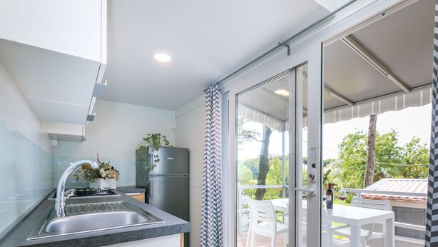 A modern kitchen with a stainless steel sink, a refrigerator, and a view of a wooden deck outside.