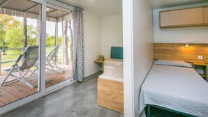 A modern bedroom with a bed, a small bedside table, and a chair. There is a sliding glass door leading to an outdoor area with a chair and a table.