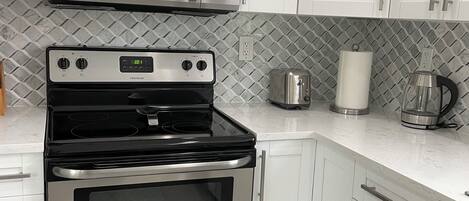 Una cocina con armarios blancos, un microondas de acero inoxidable, un horno Frigidaire y un tostador.