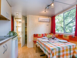 A compact kitchen with a dining area, a window with red curtains, and a table set for two with wine glasses.