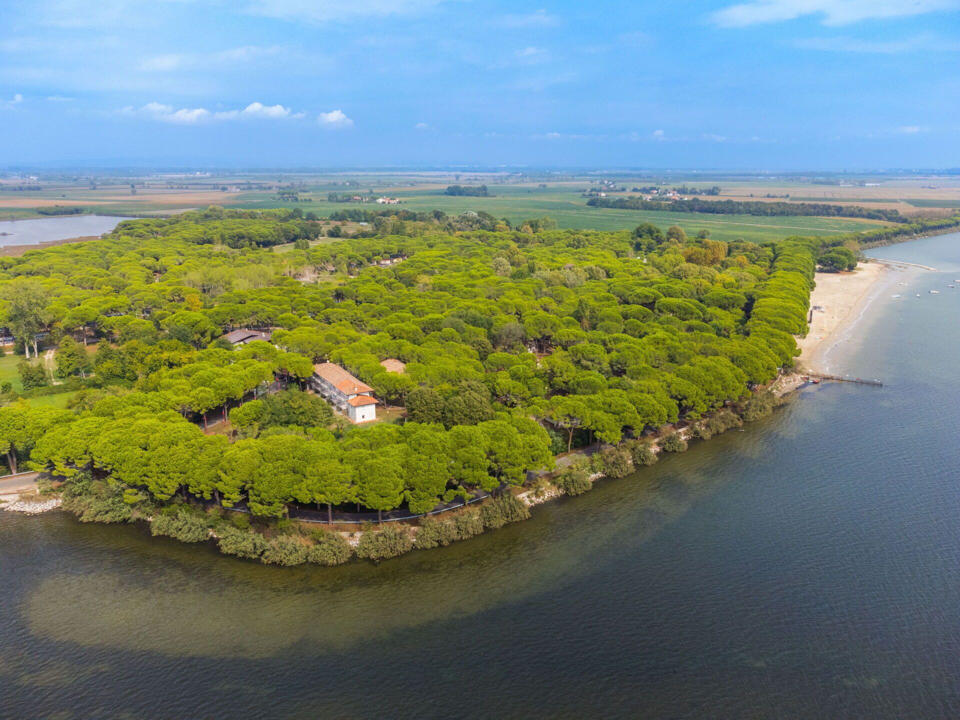 Luchtbeeld van een landgoed aan de kust, met weelderige begroeiing, een strand en een klein gebouw.