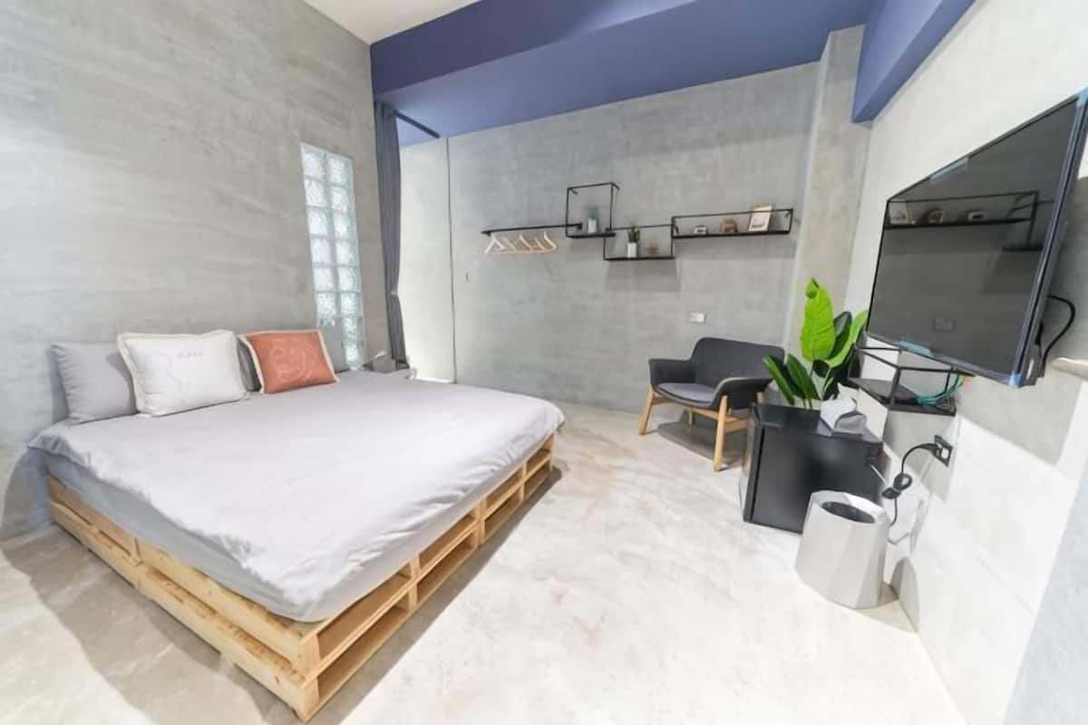 Ein modernes Schlafzimmer mit Bett, Schreibtisch, Stuhl, Fernseher und einer Pflanze.