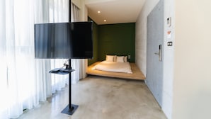 Una habitación de hotel moderna con televisión de pantalla plana, cama con ropa blanca y una pared de acento verde.