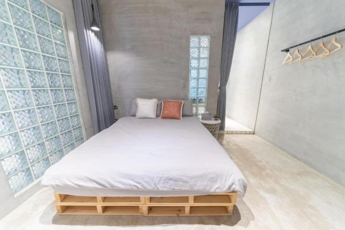 A bedroom with a wooden platform bed, a window with patterned glass, and a hanging clothes rack.