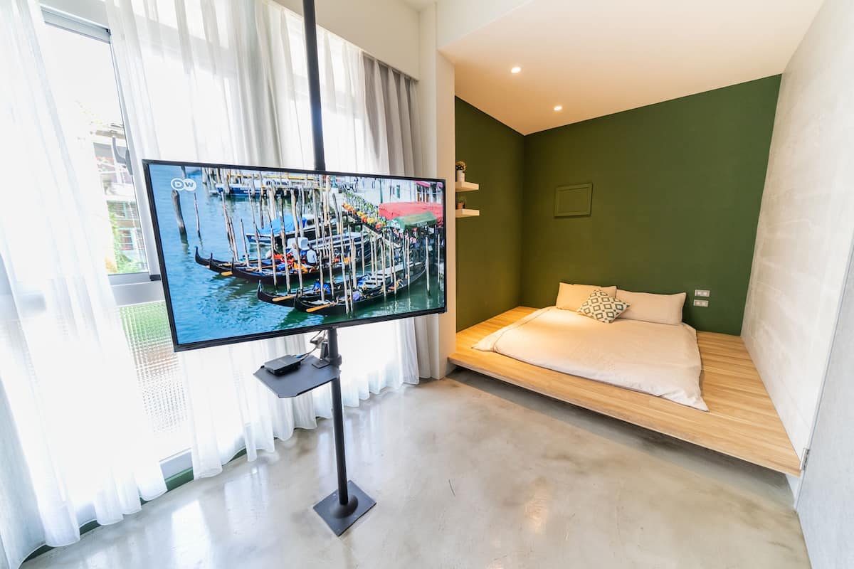 Ein modernes Hotelzimmer mit Bett, Fernseher, der eine schöne Aussicht zeigt, und einem Fenster mit transparenten Vorhängen.
