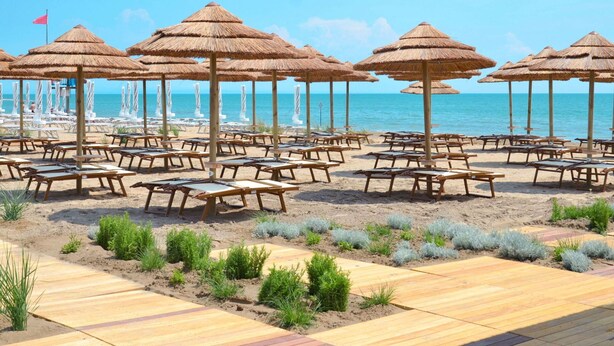 A beachside area with rows of sun loungers and thatched umbrellas, a wooden deck, and a view of the ocean. - Cosy apartment for 5 people with pool, A/C, WIFI, TV, terrace and pets allowed (San Michele Al Tagliamento)