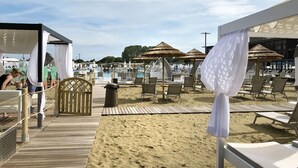 A beachside resort with a wooden deck, lounge chairs, and thatched umbrellas. - Cosy apartment for 7 people with A/C, WIFI, pool, TV, terrace and pets allowed (San Michele Al Tagliamento)