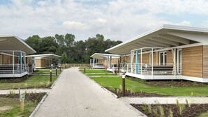 A pathway leading to modern, covered structures with wooden facades, surrounded by greenery and trees. - Cosy apartment for 7 people with A/C, WIFI, pool, TV, terrace and pets allowed (San Michele Al Tagliamento)