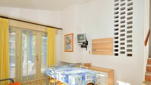 Une pièce comprenant une table à manger, des chaises, un canapé, un téléviseur et une fenêtre avec des rideaux.