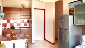 Una cocina compacta con armarios de madera, un refrigerador de acero inoxidable, una mesa de comedor con sillas y un microondas sobre una encimera.