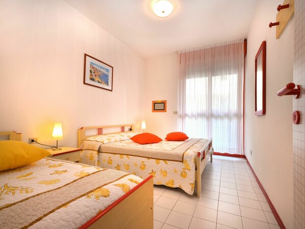A hotel room with two beds, a large window with curtains, a framed picture on the wall, and a tiled floor.
