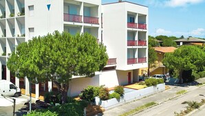 Un edificio moderno de varios pisos con balcones, rodeado de vegetación y un cielo despejado.