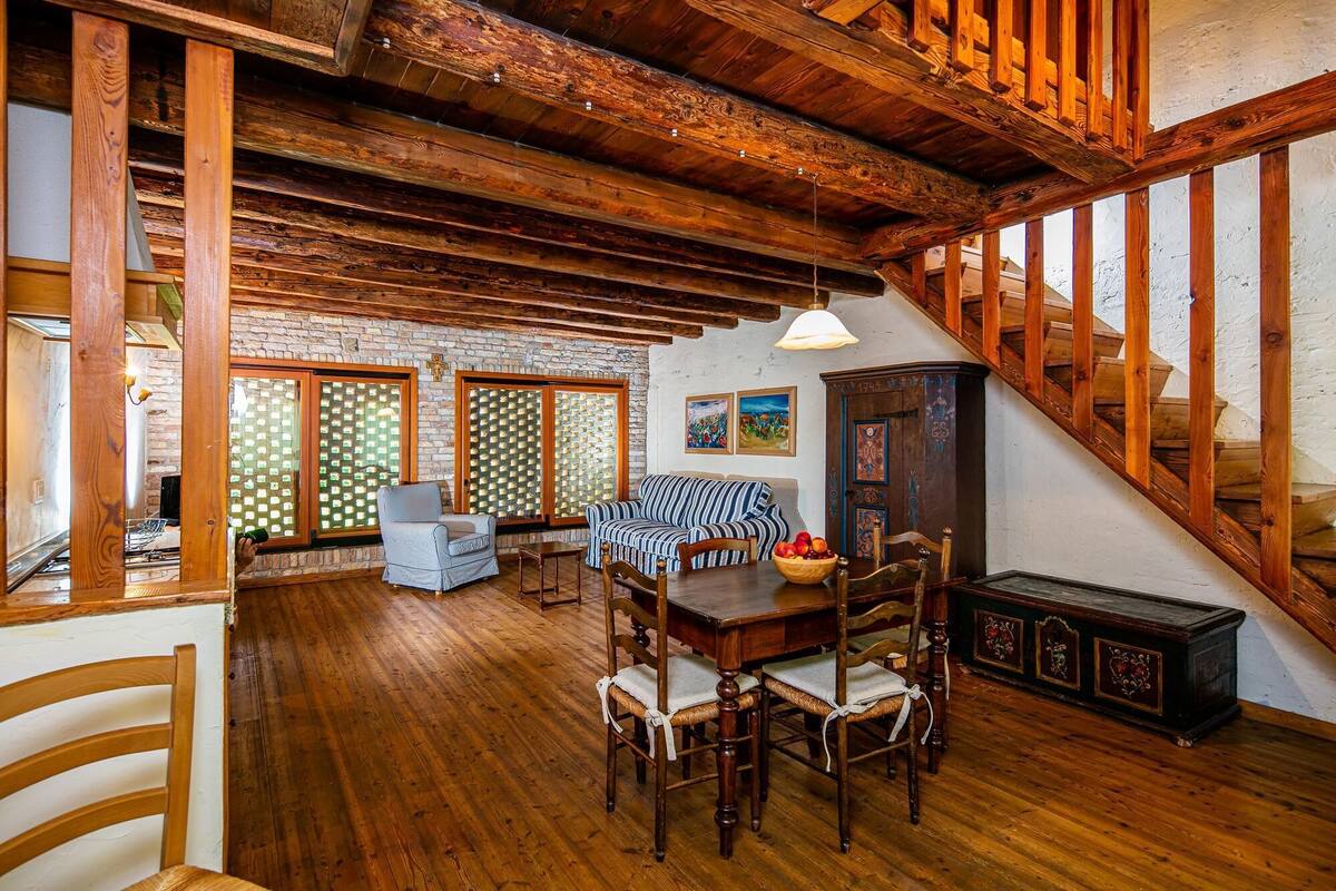 A spacious living room with wooden beams, a staircase, and a dining area with a table and chairs.