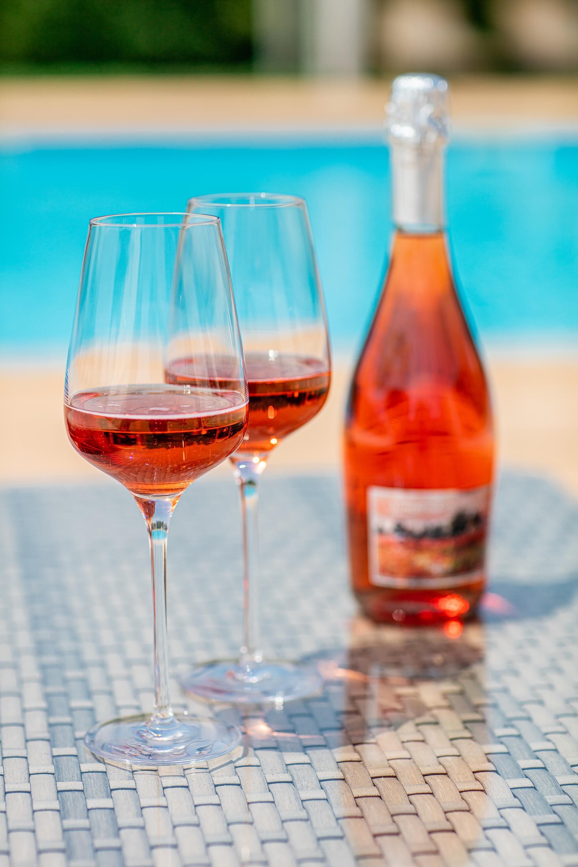 Deux verres à vin et une bouteille sont posés sur une table près d’une piscine.