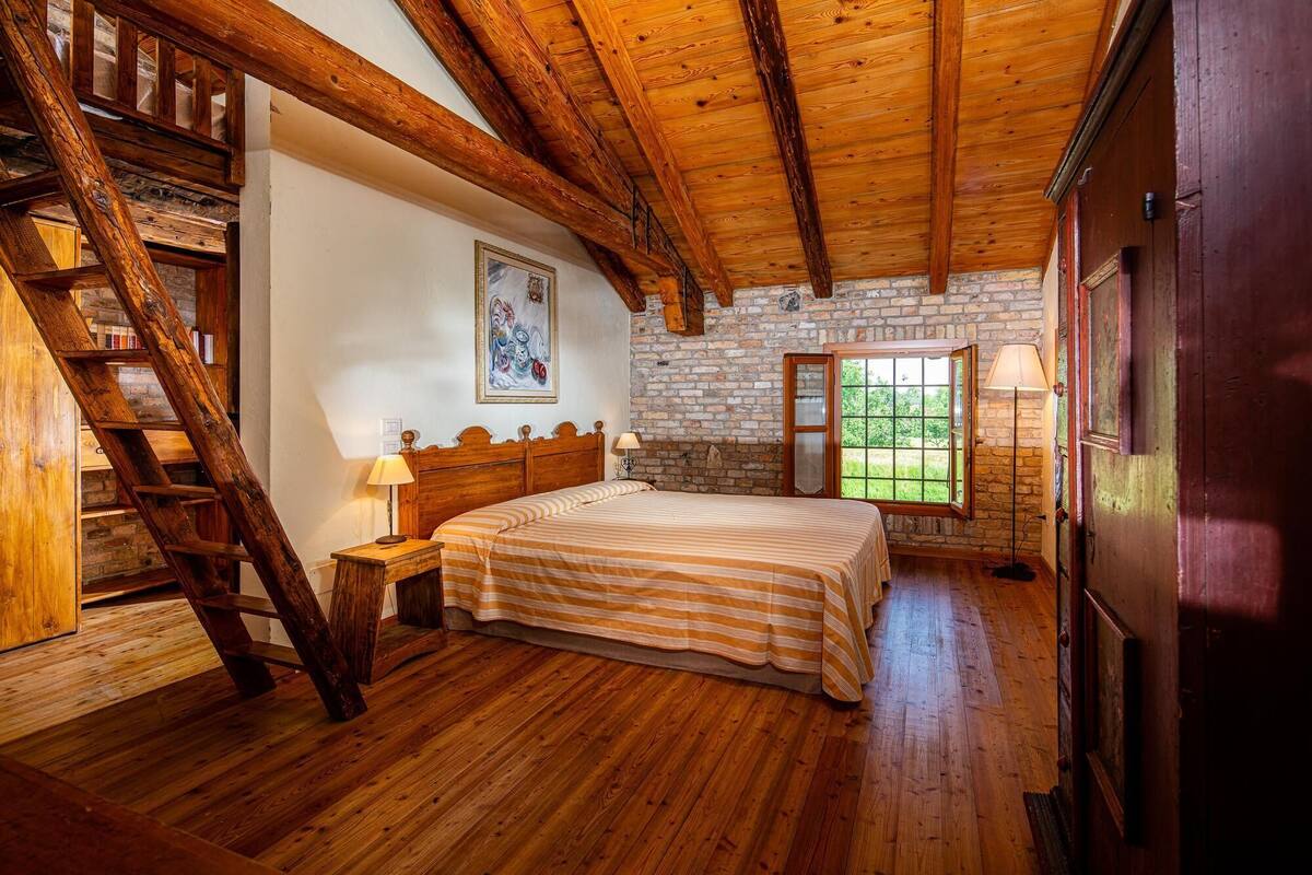 A wooden-framed bedroom with a bed, a ladder, a window with a view, and a fireplace.