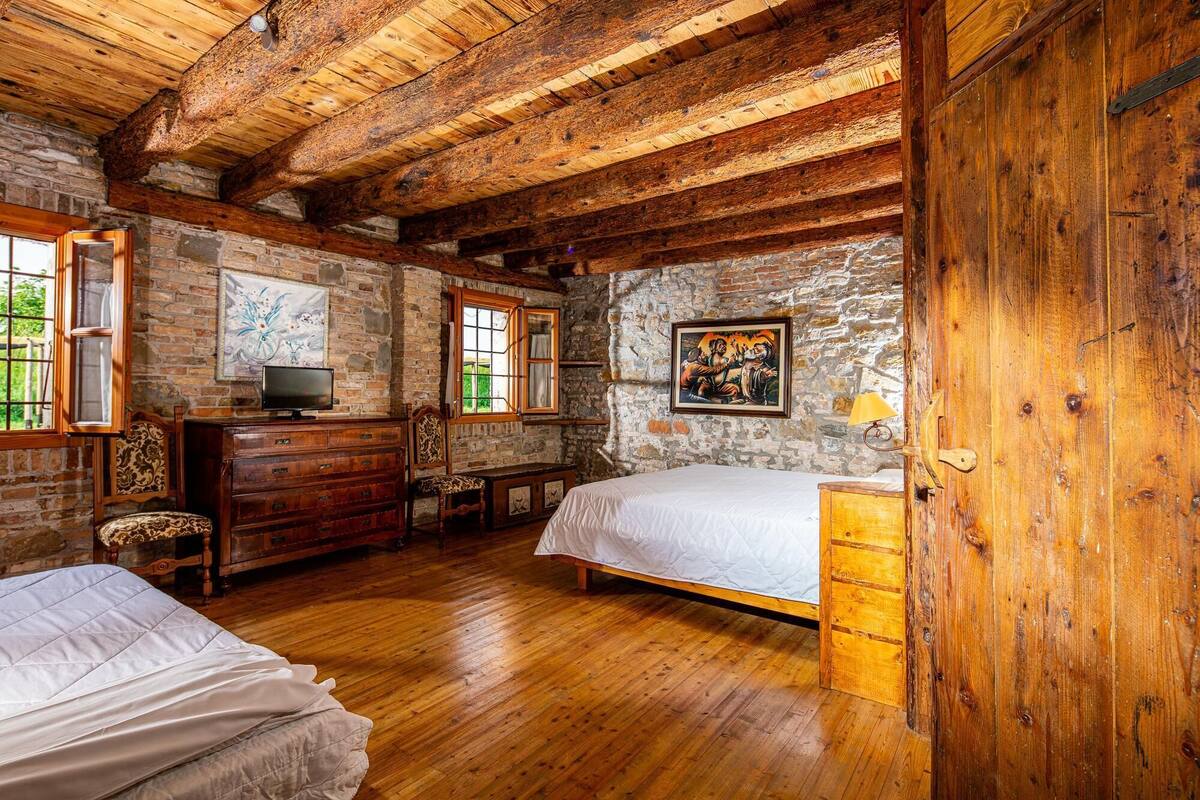A rustic wooden room with a bed, a dresser, a television, and a stone wall.
