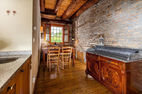 A rustic kitchen with wooden furniture, a stone wall, and a marble countertop.
