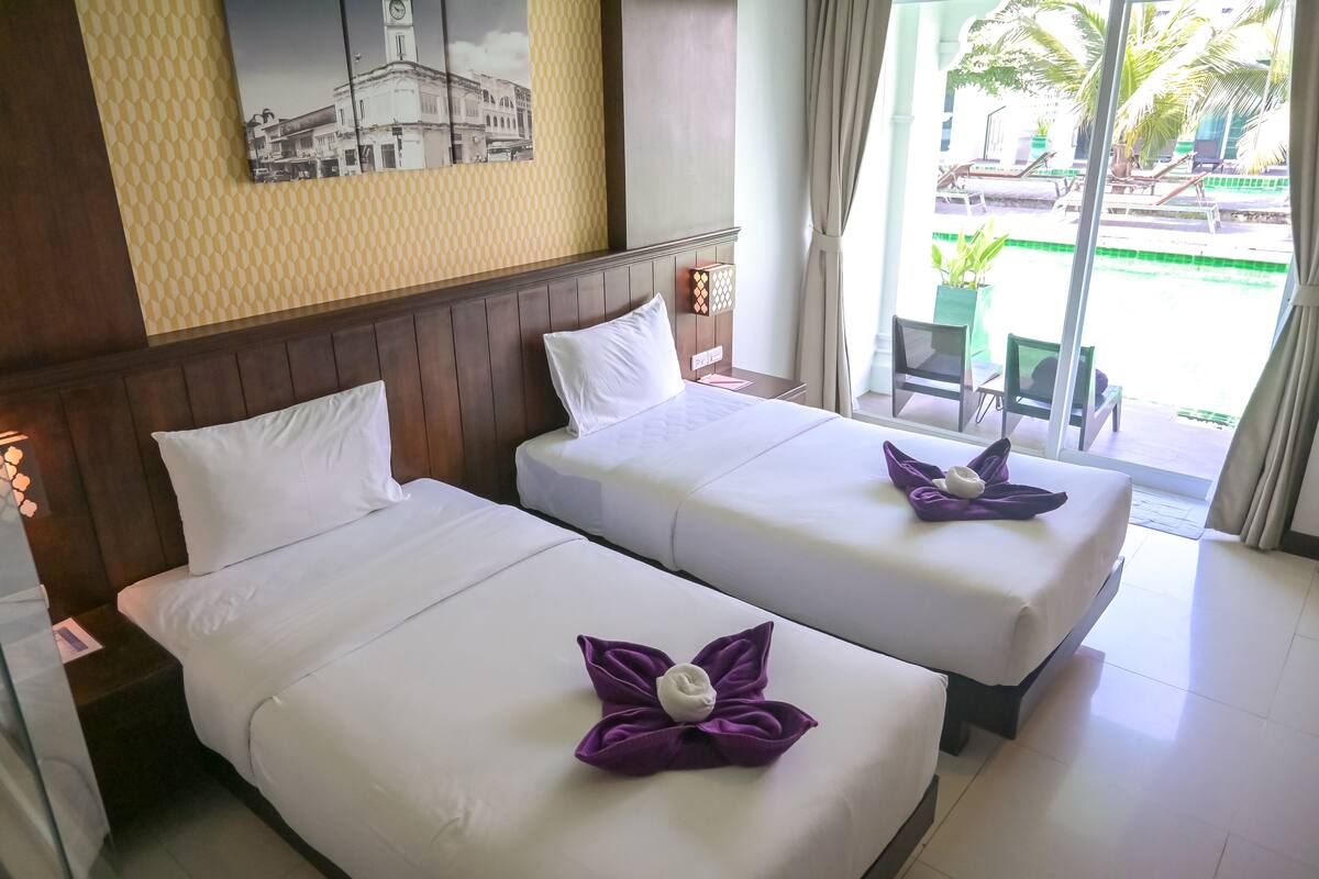 A hotel room with two beds, a wooden headboard, a wall-mounted picture, and a view of the outside.