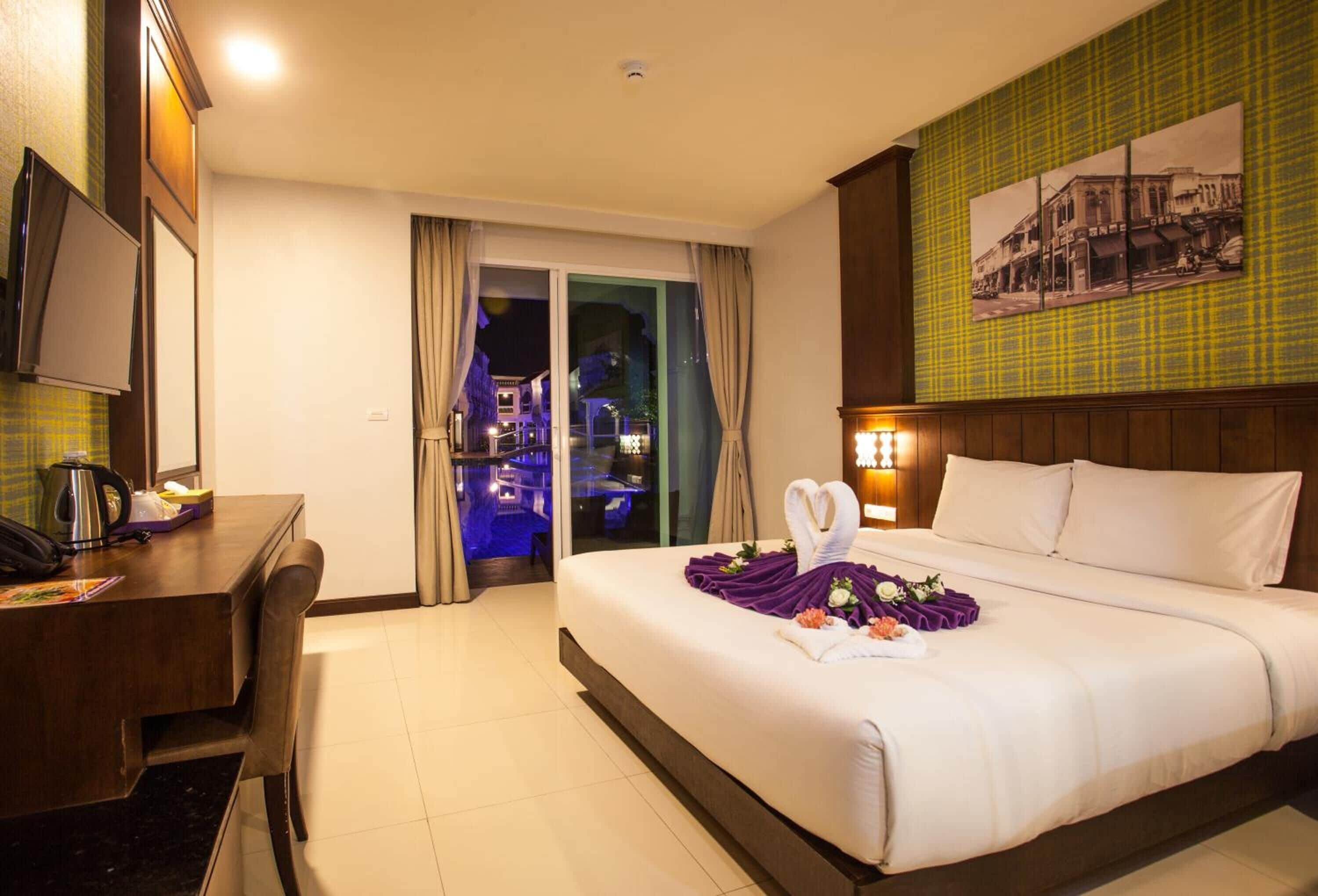 A hotel room with a bed, a desk, a chair, a television, and a view of the city at night.