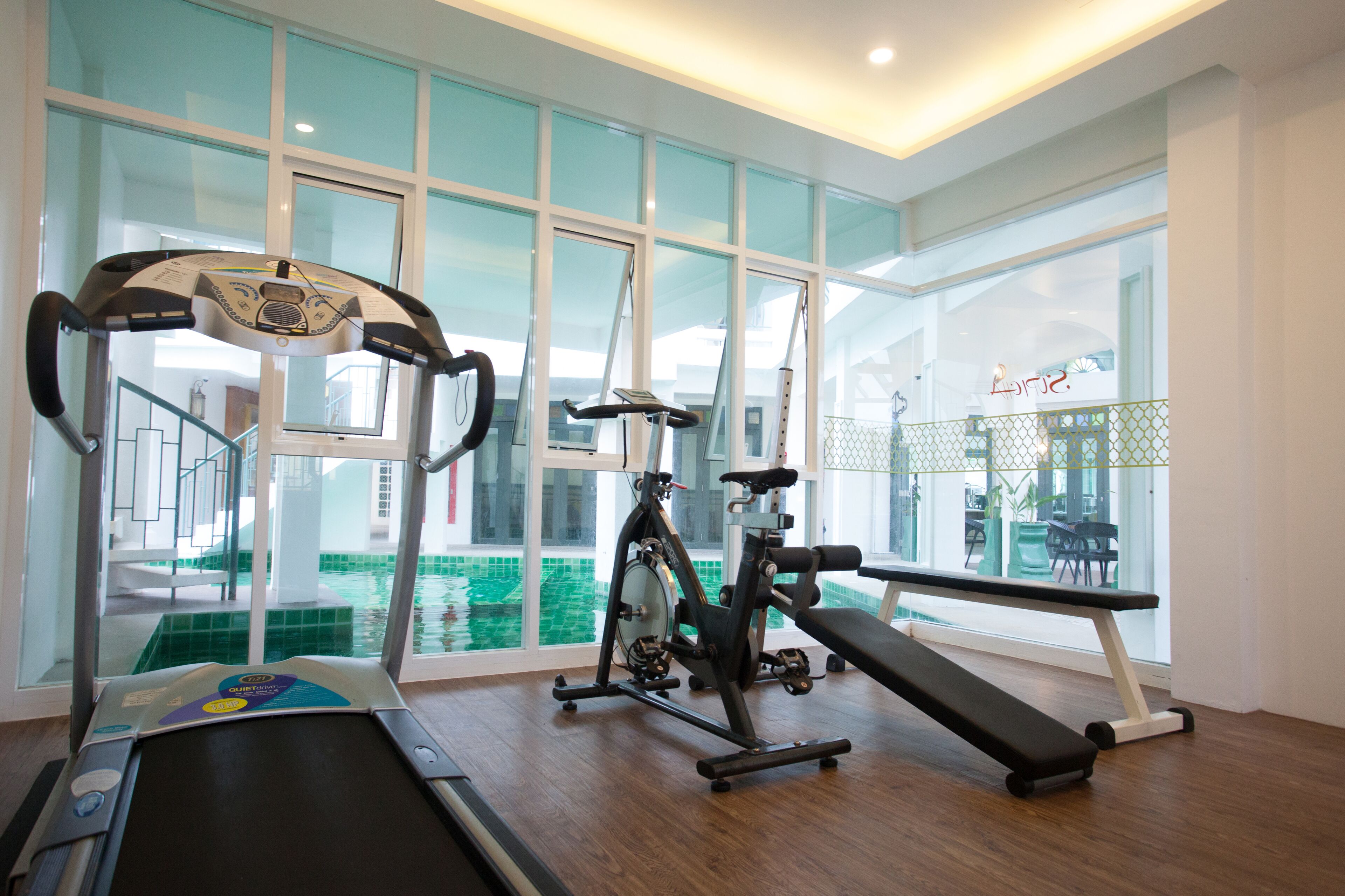A gym with cardio equipment, a bench, and a view of a swimming pool through large windows.