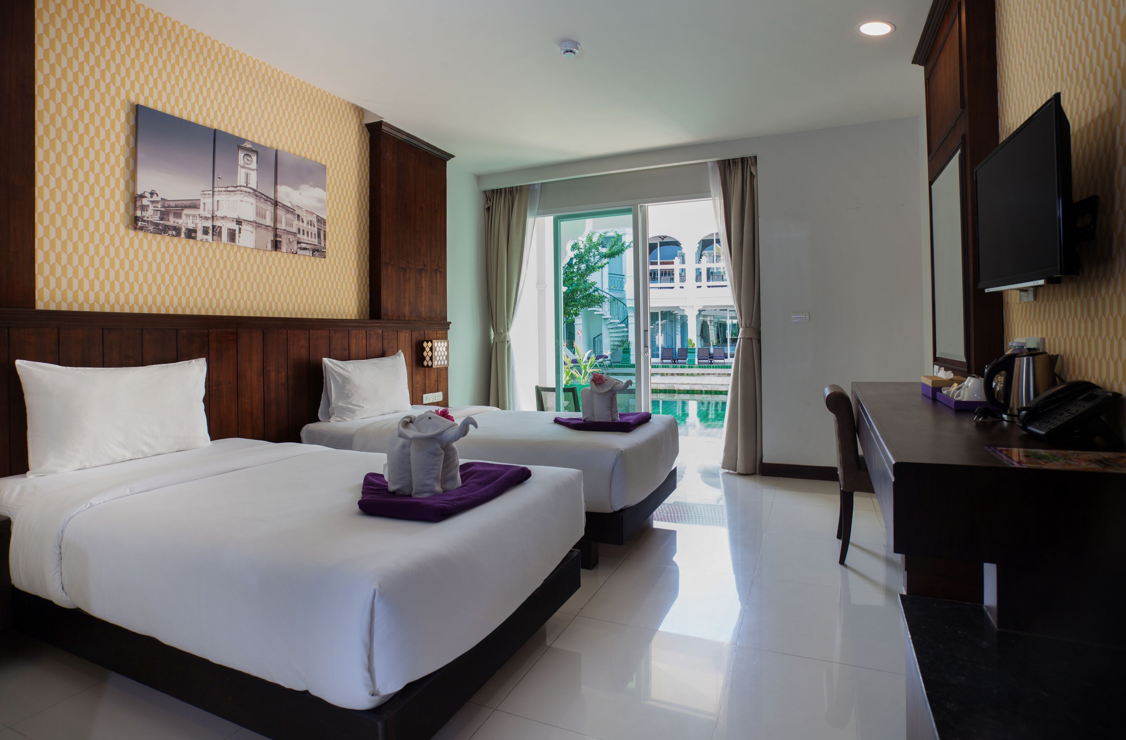 Habitación de hotel con dos camas, un escritorio, un televisor y un balcón con vistas a edificios.