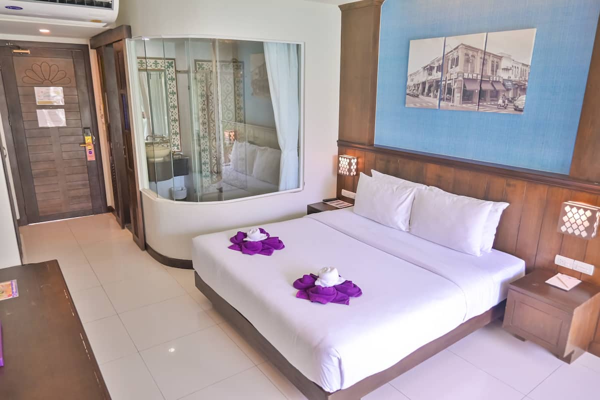 A hotel room with a large bed, a glass-enclosed bathroom, and a wall-mounted picture.