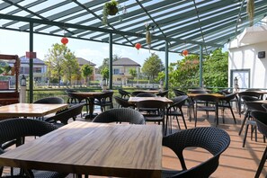 Eine Terrassenanlage mit Tischen und Stühlen, eine Pergola mit hängenden Pflanzen und im Hintergrund Wohnhäuser.